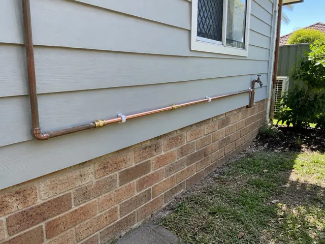 Copper water pipe repaired along exterior wall above brick base in Shortland