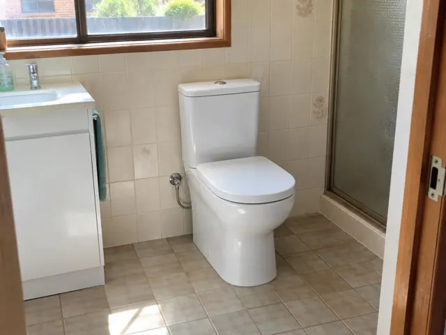 White toilet in a tiled bathroom with vanity, window and shower screen in Callaghan